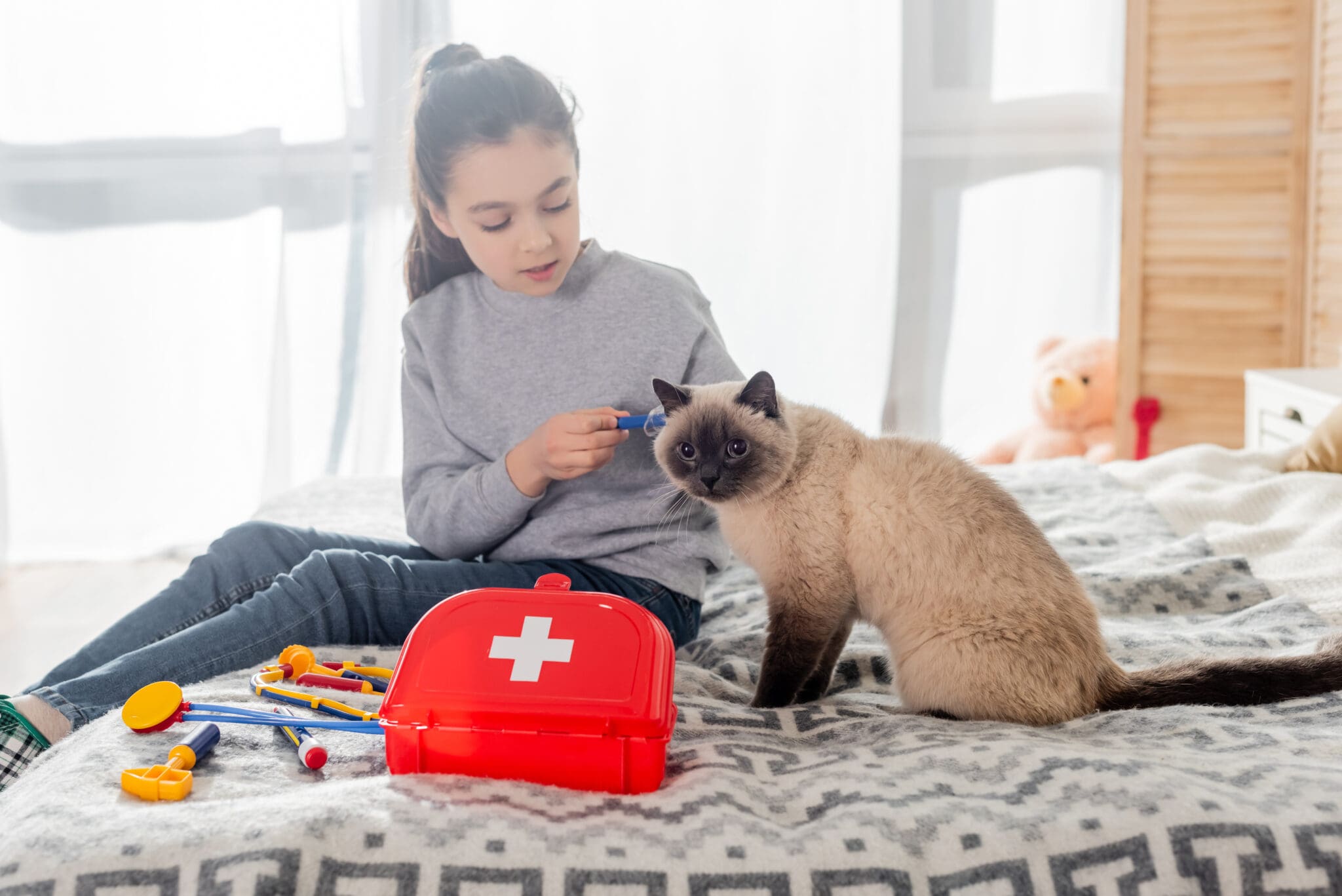 Girl Making Injection To Cat With Toy Syringe Near First Aid Kit On Bed.